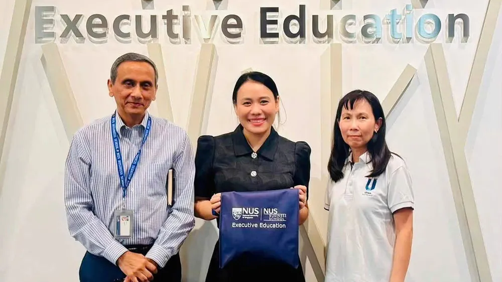 Ba người đứng trước bức tường "Executive Education", người ở giữa cầm túi NUS Business School