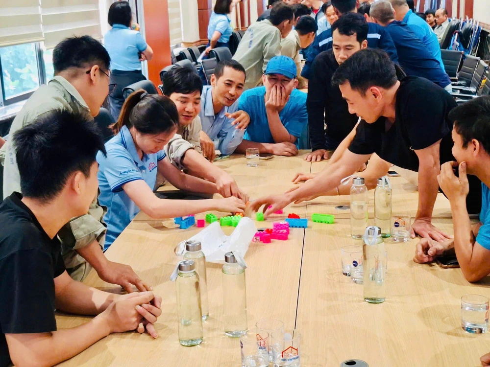 Toàn bộ nhóm ABC Việt Nam quây quanh bàn, cùng xếp mô hình bằng các khối màu; trên bàn có những chiếc cốc in chữ ABC VIETNAM