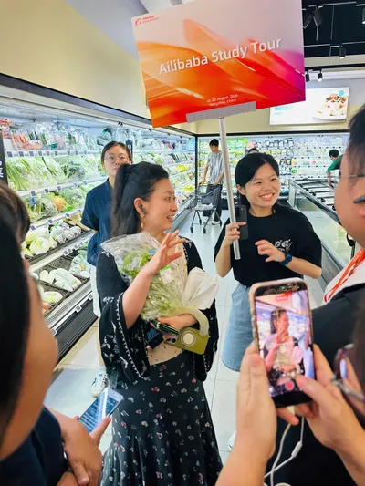 Thành viên đoàn cầm bảng Alibaba Study Tour tại khu siêu thị Hema, một người cầm hoa và một người quay điện thoại